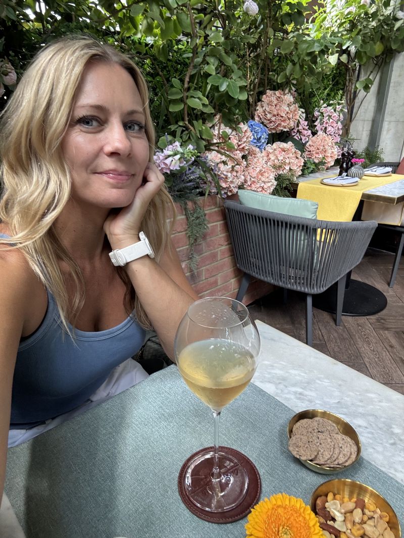 Melanie with a glass of champagne on a flower-filled terrace in London